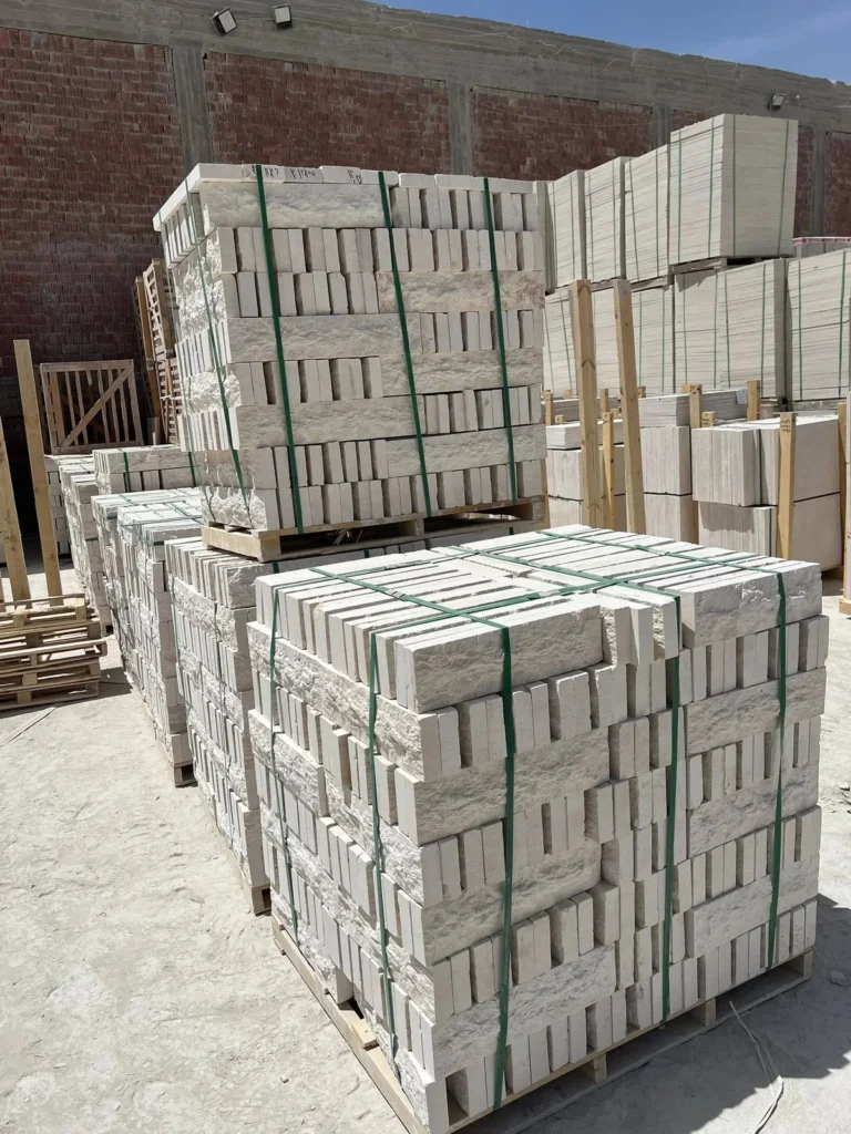 Light-coloured cut stone stacked and strapped on wooden pallets in an outdoor yard.