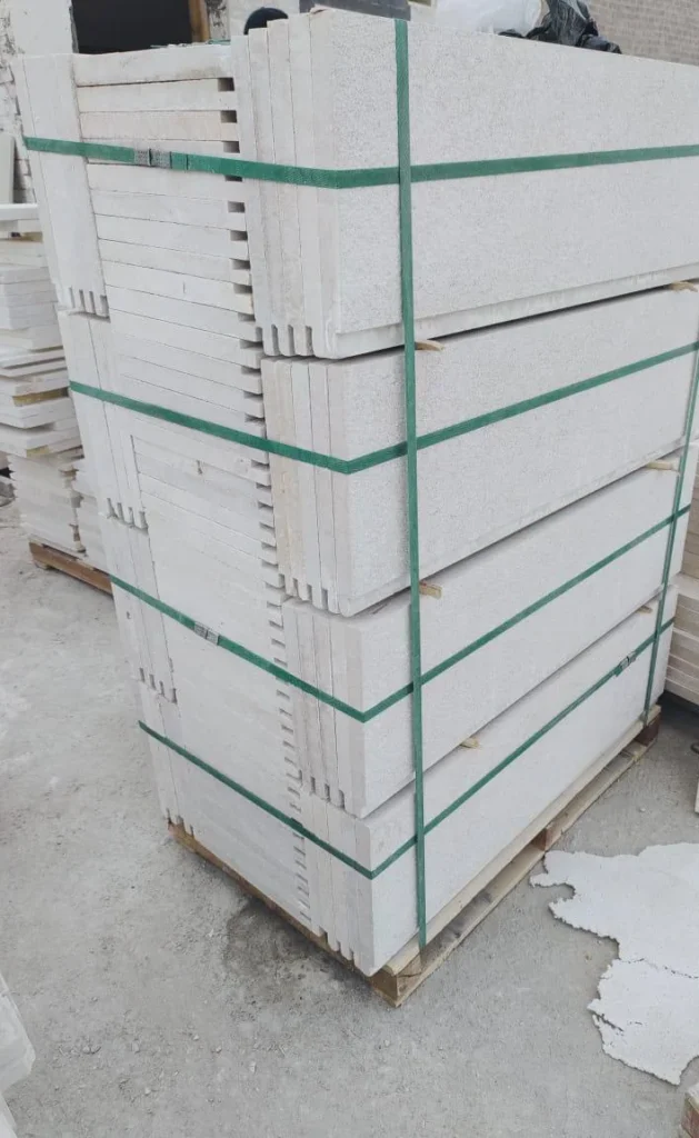 Pale cut-stone pieces secured with green straps on a wooden pallet.
