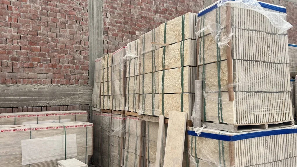 Stacks of light-coloured cut stone secured with straps and plastic wrap in a storage yard.