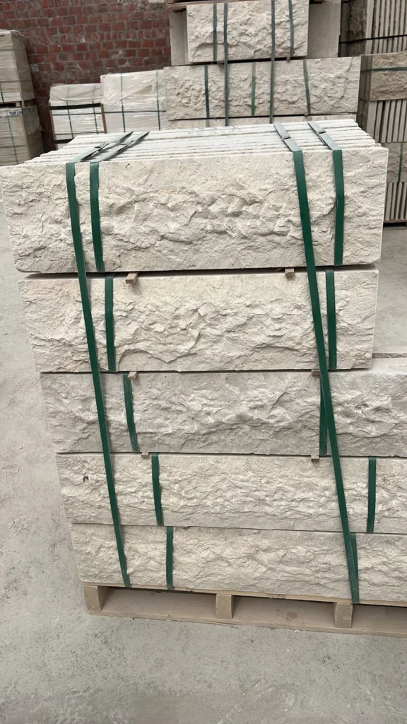 Strapped stacks of light-coloured stone pieces with rough, uneven faces.