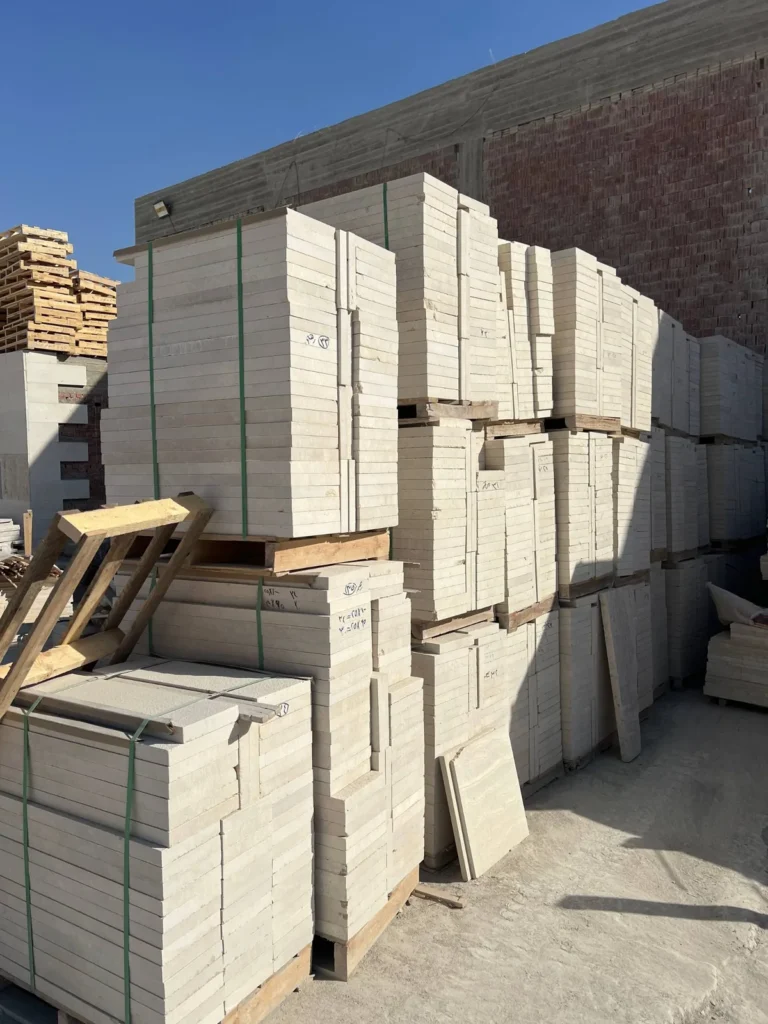 Tall stacks of pale cut stone on wooden pallets in a sunlit storage yard.