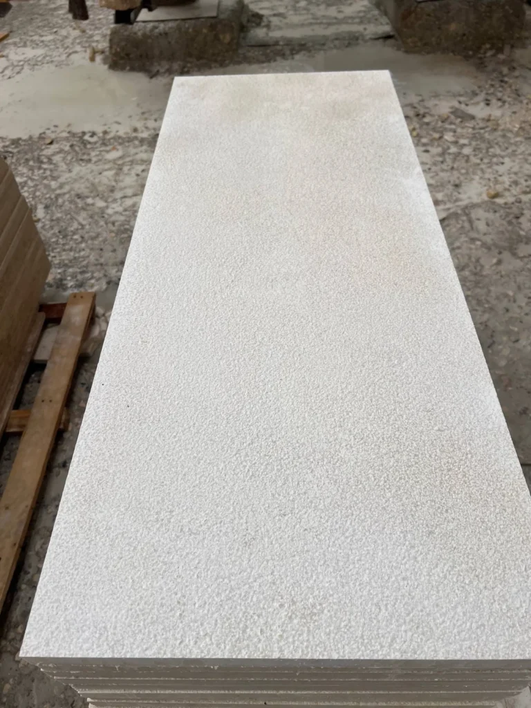 Close view of a pale, finely textured rectangular stone piece above a stack of matching pieces.