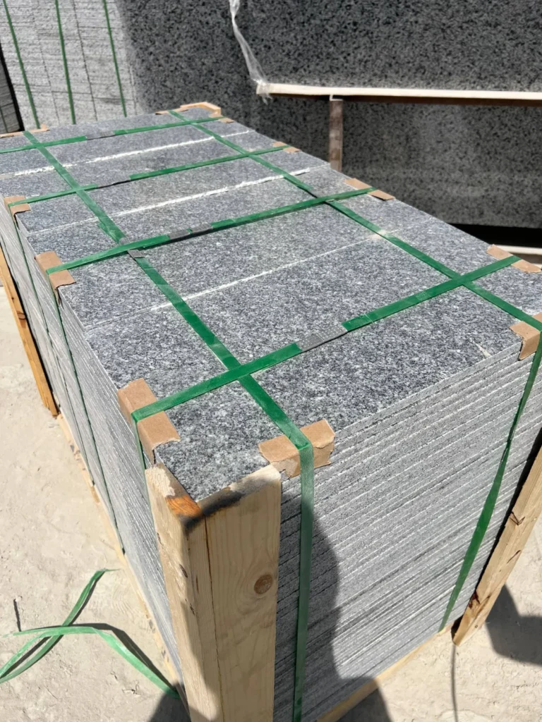 Speckled cut-stone pieces stacked with corner protectors and green straps on a wooden pallet.