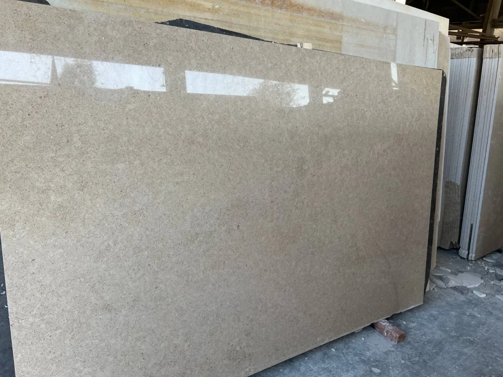 Broad grey-beige stone slab reflecting overhead light in front of stacked slabs.