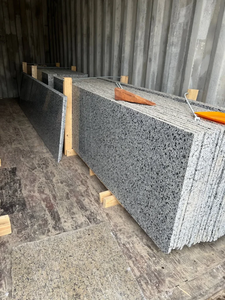 Upright speckled stone slabs supported by timber and metal restraints inside a shipping container.