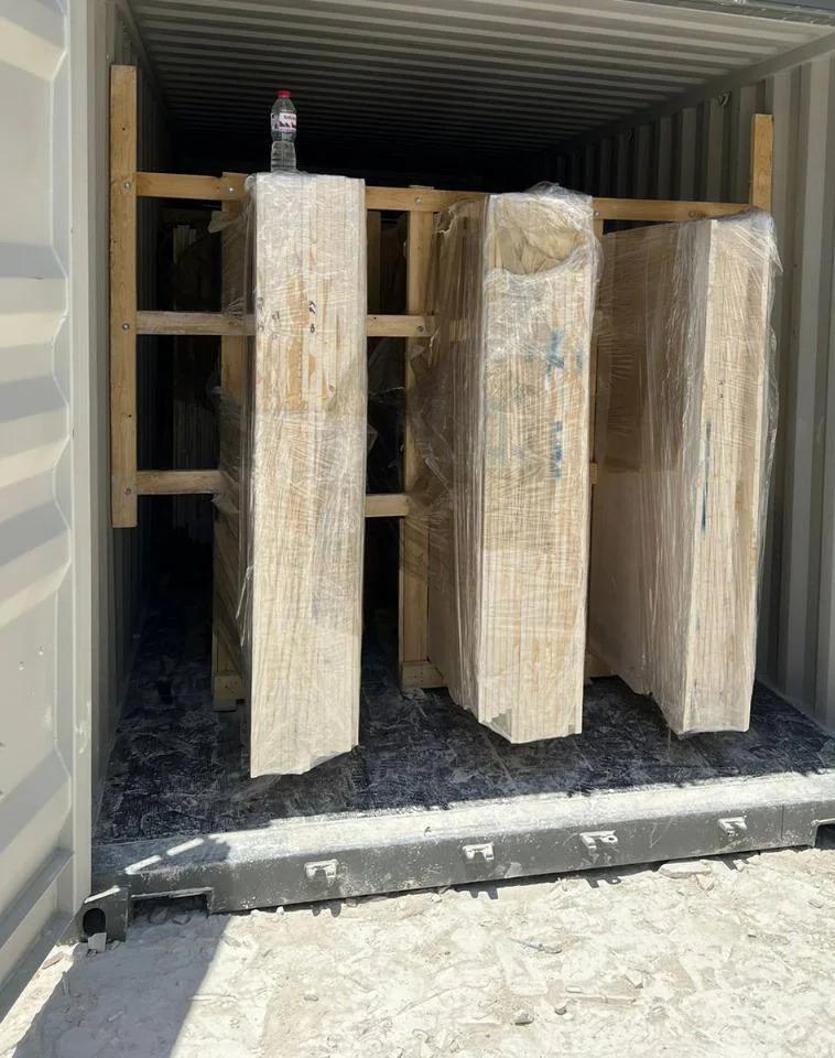 Wrapped upright stone packages in timber supports inside an open shipping container.