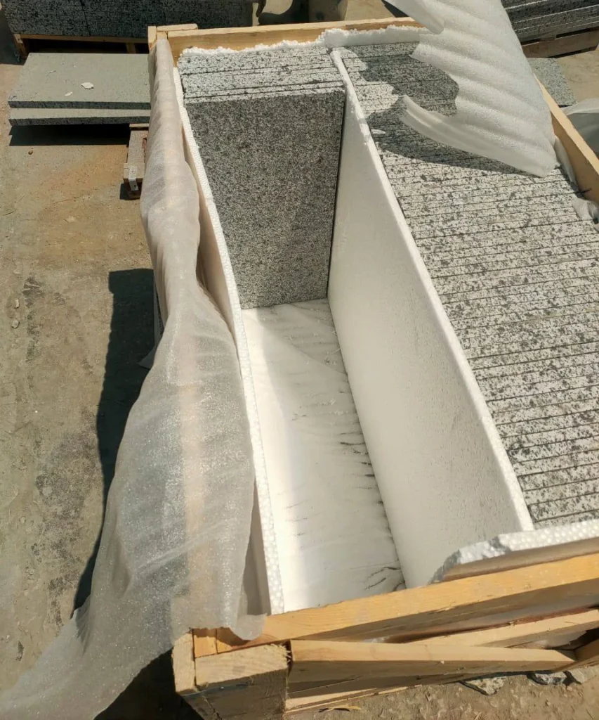 Open wooden crate holding speckled stone pieces with white separators and protective wrapping.