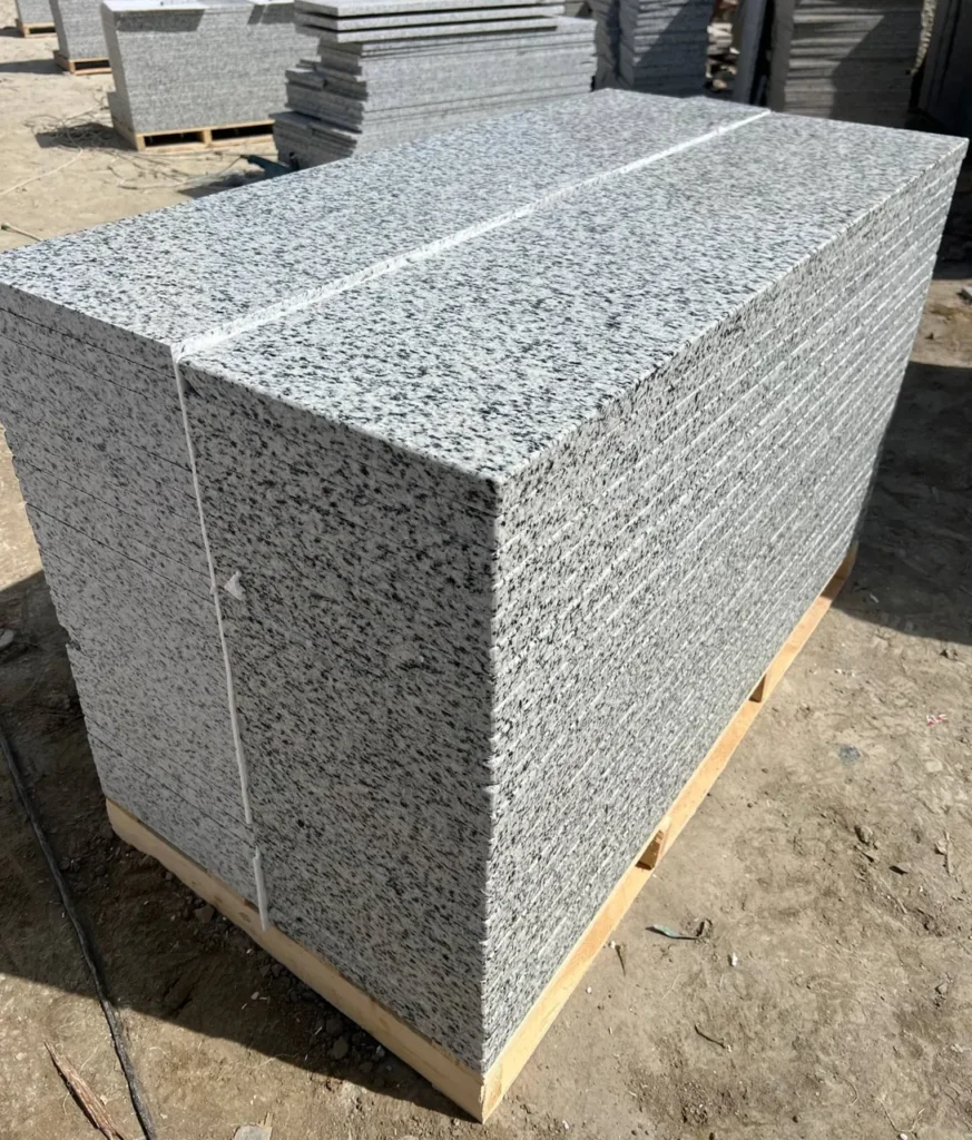 Stack of grey-and-black speckled stone tiles on a wooden pallet in a stone yard.