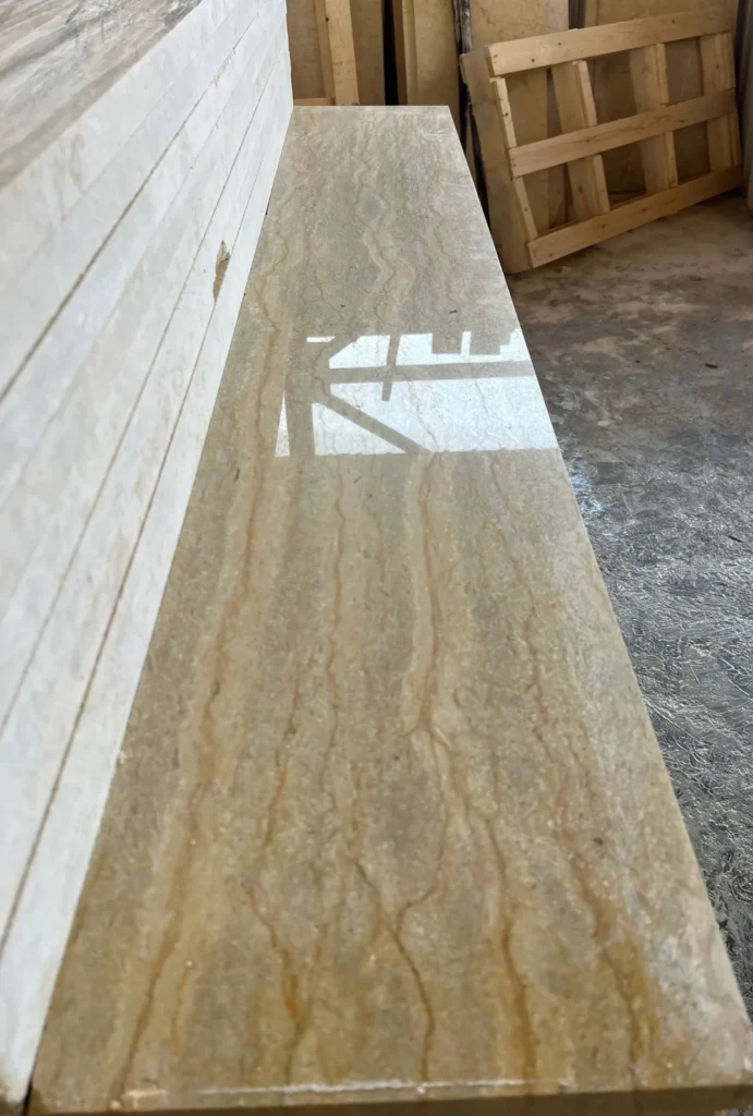 Long glossy beige stone piece with fine wavy brown veins beside a stack of pale pieces.