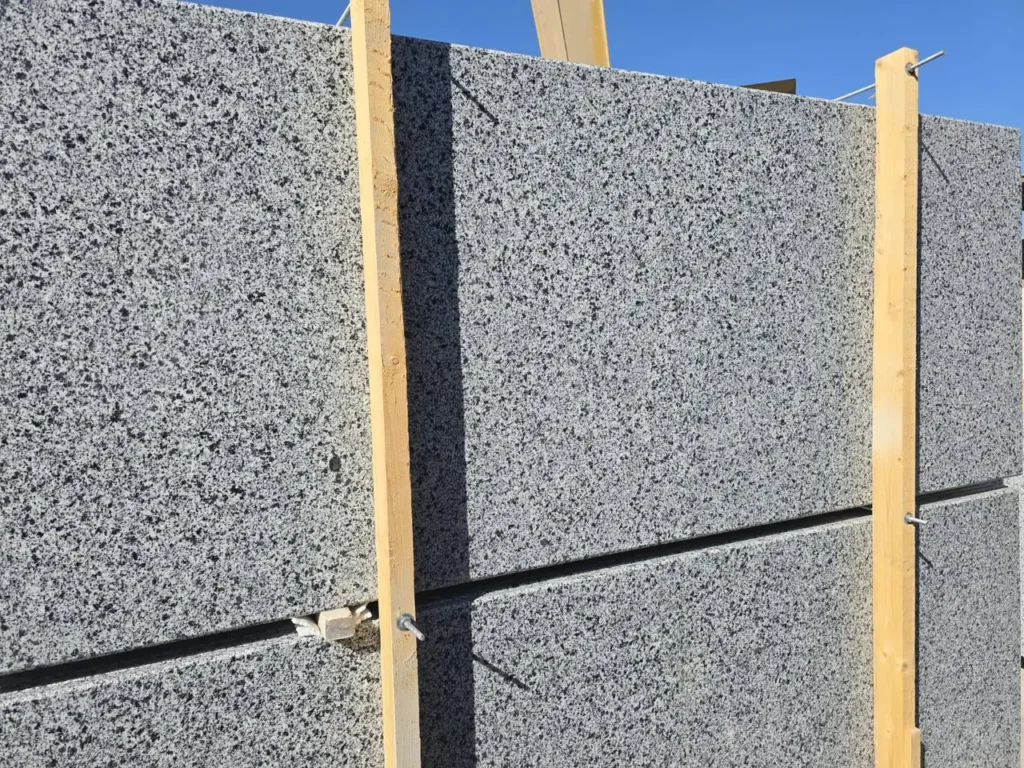 Close view of black-and-white speckled stone slabs stacked behind timber uprights outdoors.