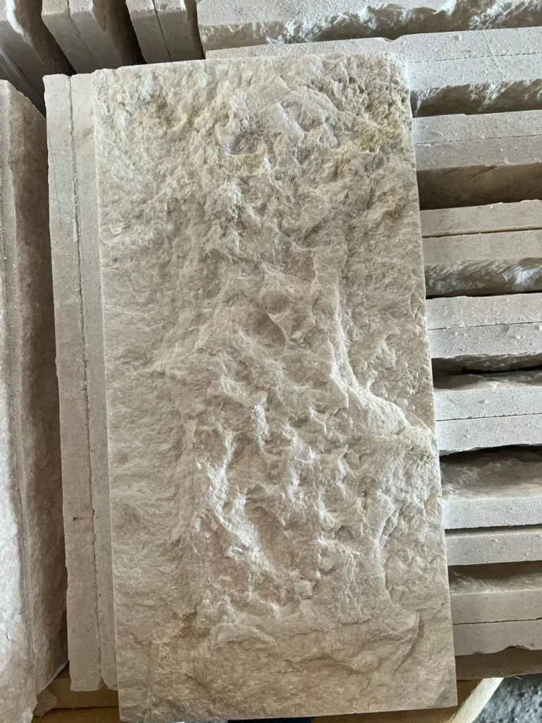 Pale stone piece with a deeply rough, irregular textured face in front of other stacked pieces.
