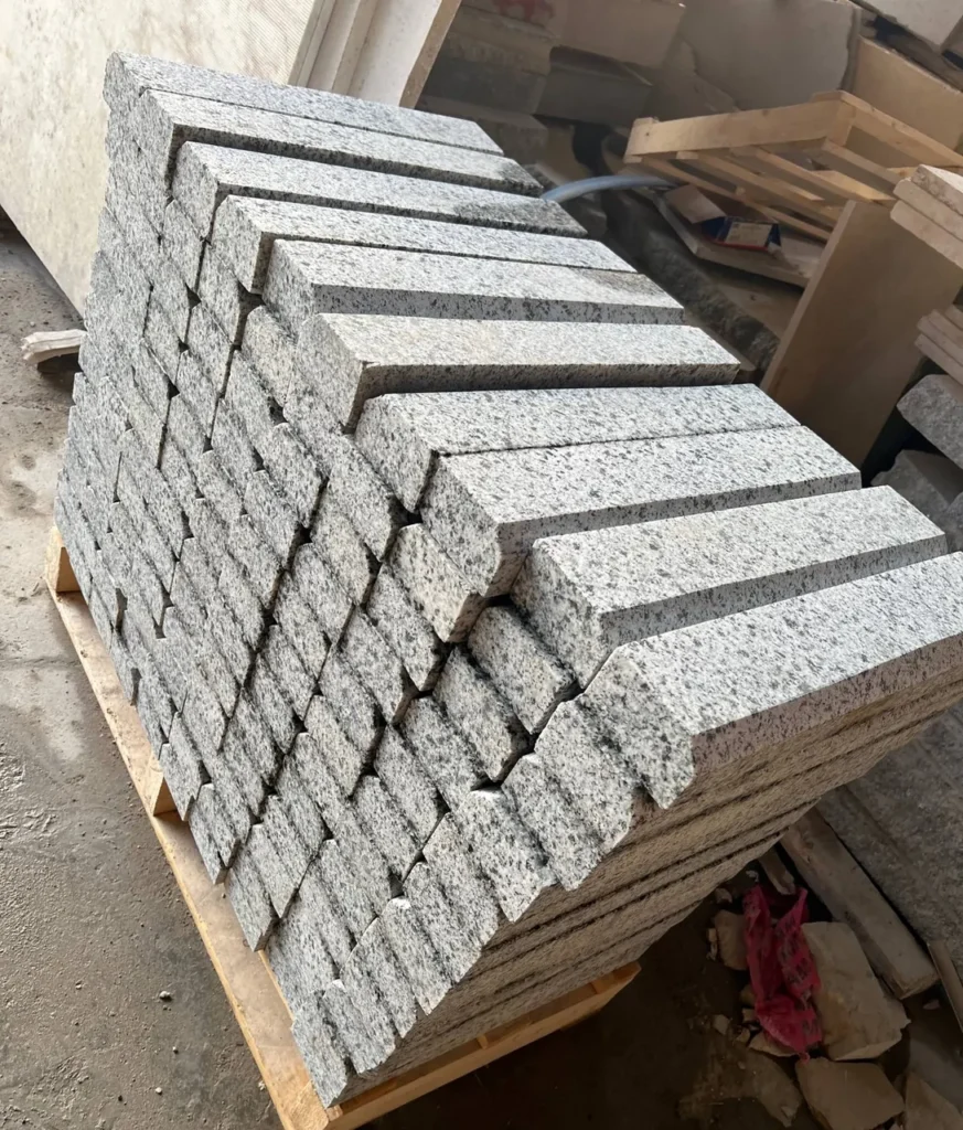 Rows of long narrow speckled stone pieces stacked at an angle on a wooden pallet.