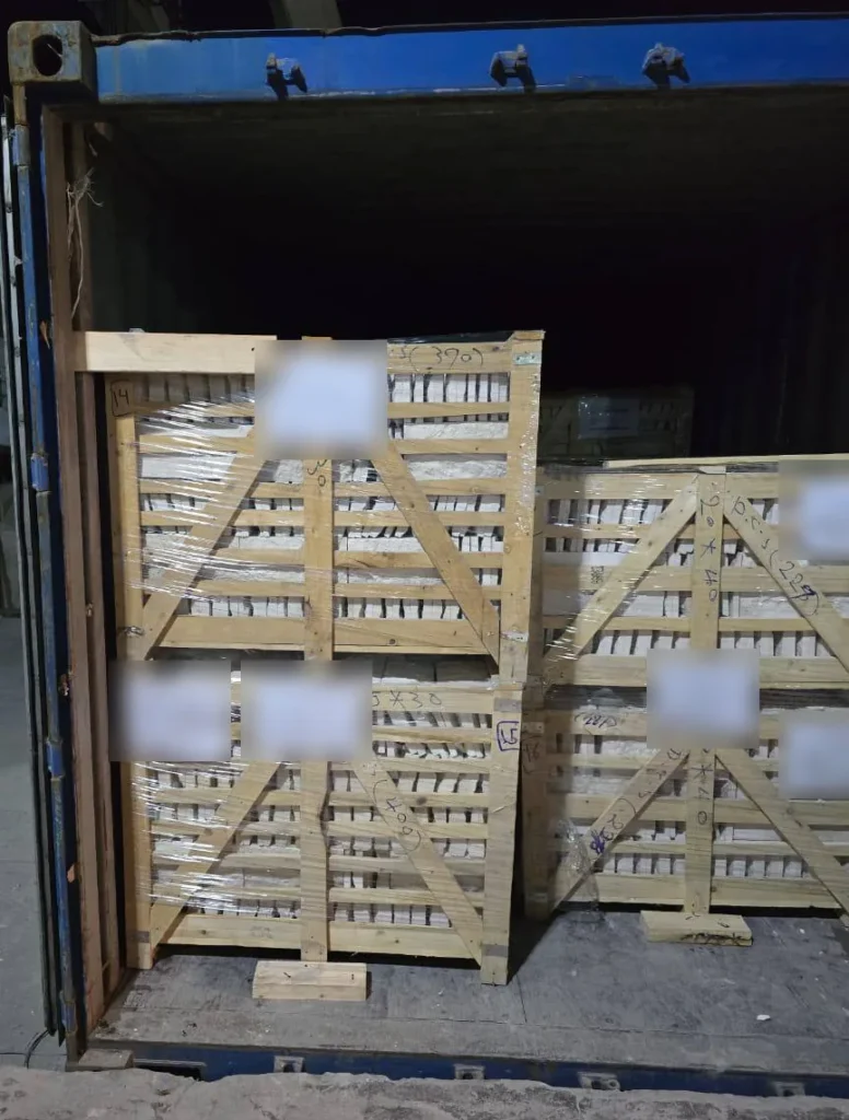 Wrapped timber-framed stone packages at the entrance of a blue-framed shipping container.