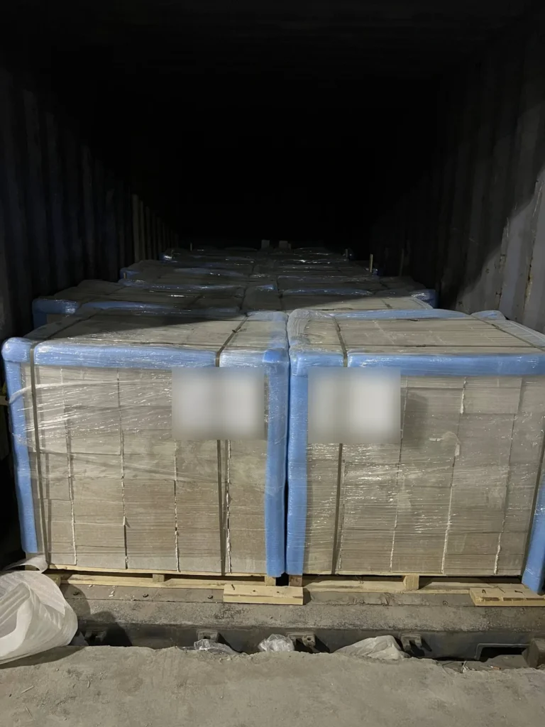 Rows of wrapped stone packages with blue corner guards extending into a dark shipping container.